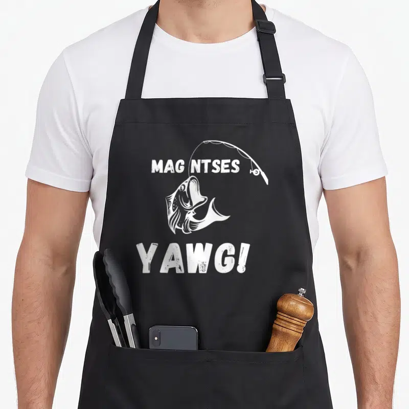 Tablier de cuisine noir avec illustration blanche d'un poisson sautant sous une canne à pêche et le texte Mag ntses yawg.