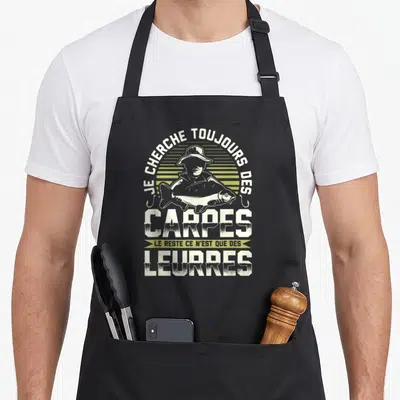 Tablier de cuisine noir avec illustration d'un pêcheur tenant une carpe et texte humoristique sur la pêche.
