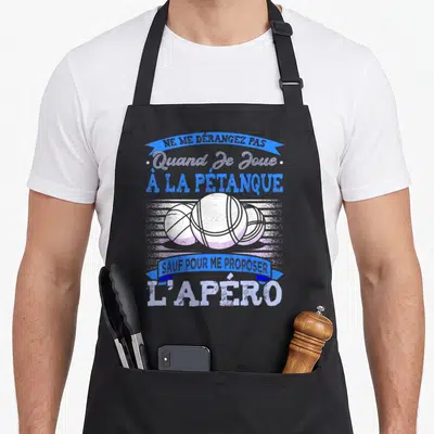 Tablier de cuisine noir avec trois boules de pétanque blanches et texte humoristique en bleu et blanc sur fond gris strié.