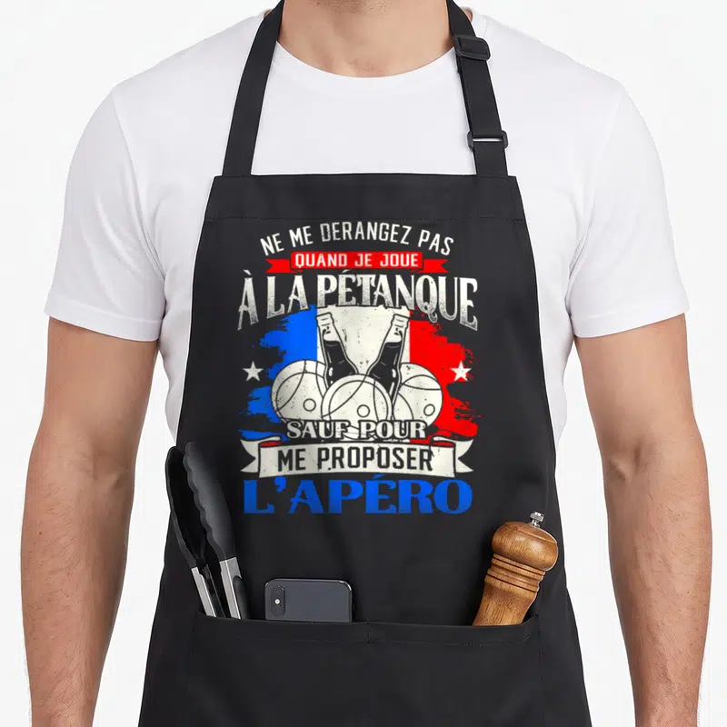 Tablier de cuisine noir avec illustration de boules de pétanque, bières et texte humoristique sur fond aux couleurs du drapeau français.
