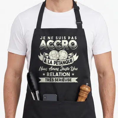 Tablier de cuisine noir avec inscription humoristique sur la passion pour la pétanque et deux boules métalliques stylisées.