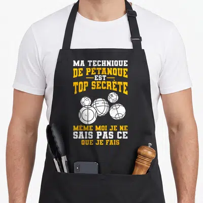 Tablier de cuisine noir avec inscription Ma technique de pétanque est top secrète et illustration de cinq boules blanches stylisées.