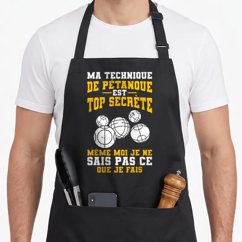 Tablier de cuisine noir avec inscription Ma technique de pétanque est top secrète et illustration de cinq boules blanches stylisées.