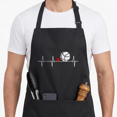 Tablier de cuisine noir avec un motif blanc représentant un électrocardiogramme intégrant une petite boule rouge et une grande boule texturée.