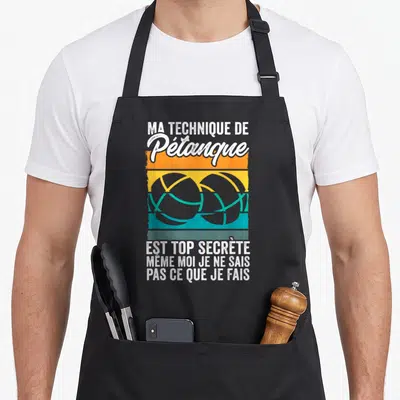 Tablier de cuisine noir avec inscription blanche Ma Technique De Pétanque Est Top Secrète et illustration de deux boules de pétanque sur bandes orange jaune turquoise.