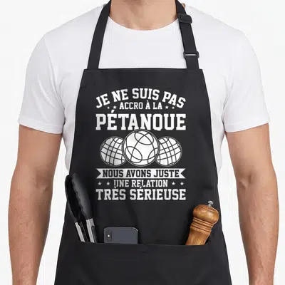 Tablier de cuisine noir avec trois boules de pétanque blanches et un texte humoristique sur le devant.