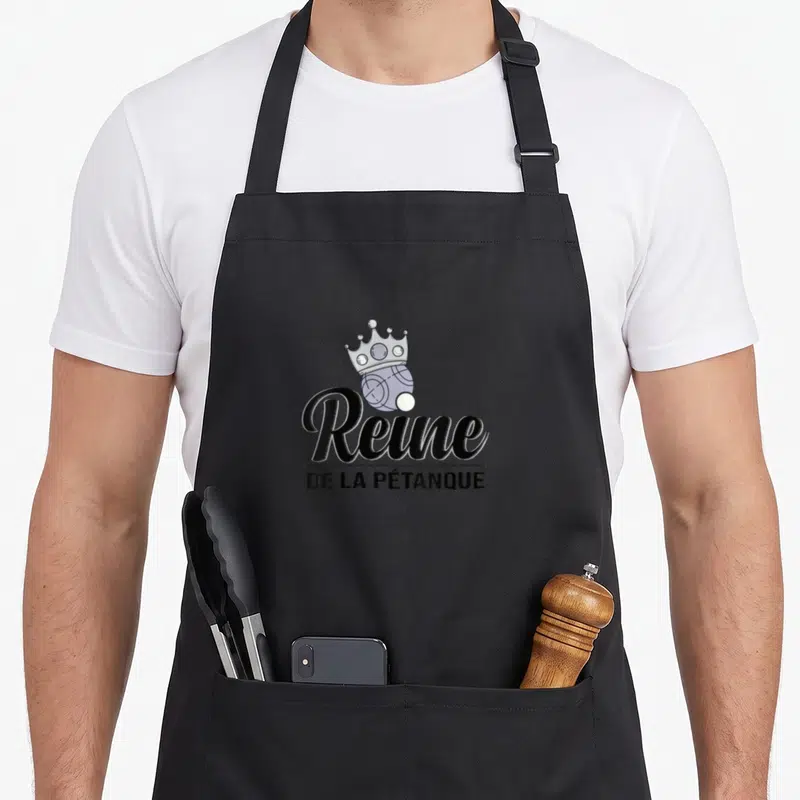 Tablier de cuisine noir avec une boule surmontée d'une couronne et le texte Reine de la Pétanque en typographie élégante.