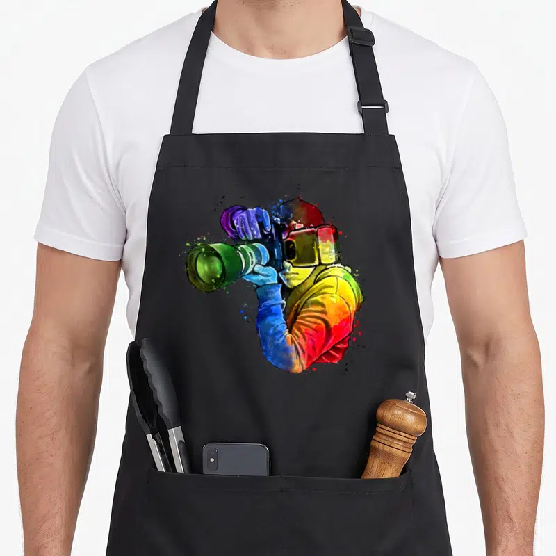 Tablier de cuisine noir avec illustration d'un photographe en aquarelle multicolore tenant un appareil photo.