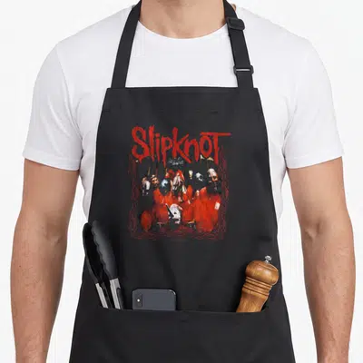 Tablier de cuisine noir avec illustration groupe Slipknot logo rouge et membres masqués tenues oranges encadrés motifs ornementaux.