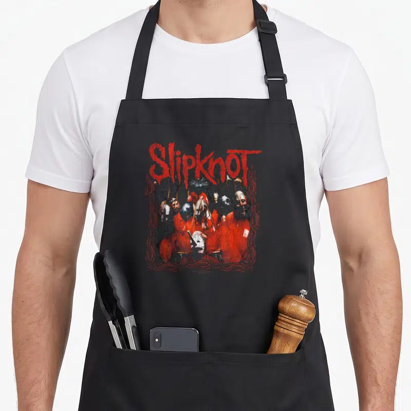 Tablier de cuisine noir avec illustration groupe Slipknot logo rouge et membres masqués tenues oranges encadrés motifs ornementaux.