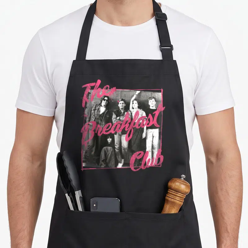 Tablier de cuisine noir avec photo de groupe en noir et blanc et texte rose The Breakfast Club superposé.