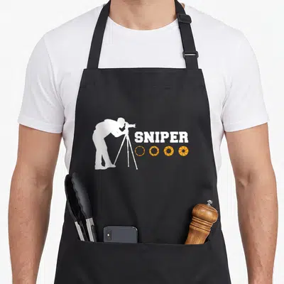 Tablier de cuisine noir avec silhouette blanche photographe trépied texte sniper et quatre diaphragmes oranges alignés.
