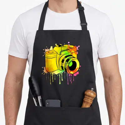 Tablier de cuisine noir avec un appareil photo jaune et des éclaboussures de peinture multicolores.