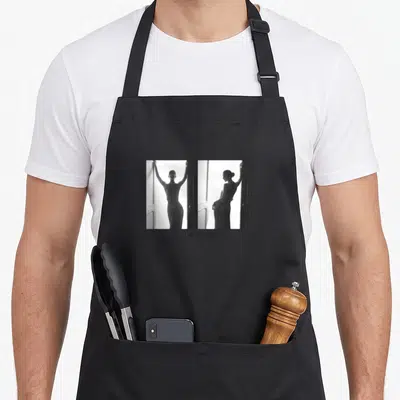 Tablier de cuisine noir avec deux silhouettes Celine Dion en noir et blanc et le nom imprimé en bas.