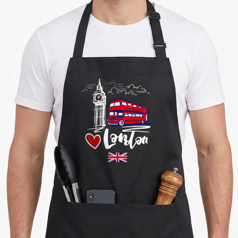 Tablier de cuisine noir avec illustration de bus rouge, Big Ben, cœur rouge et drapeau britannique sous le texte I Love London.