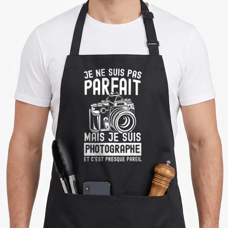 Tablier de cuisine noir avec illustration de caméra et texte blanc sur fond uni.