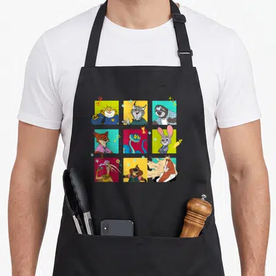 Tablier de cuisine noir avec une grille de neuf cases colorées représentant des personnages animaux stylisés et des objets comme des clés ou des carottes.
