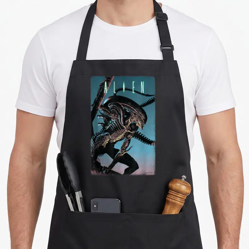 Tablier de cuisine noir avec illustration du Xenomorph et le mot ALIEN en lettres vertes sur fond dégradé bleu.