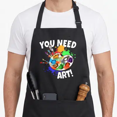 Tablier de cuisine noir avec une palette de peintre, des pinceaux et le texte You Need Art en lettres blanches.