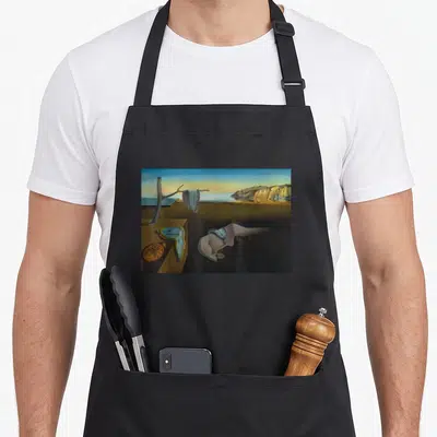 Tablier de cuisine noir avec reproduction de La persistance de la mémoire de Dali montrant des montres molles sur un paysage désertique.