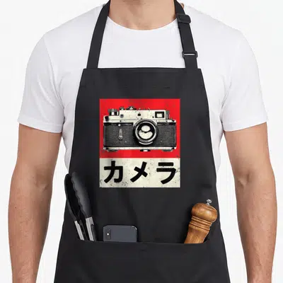 Tablier de cuisine noir avec illustration d'un appareil photo vintage sur fond rouge et caractères japonais en bas.