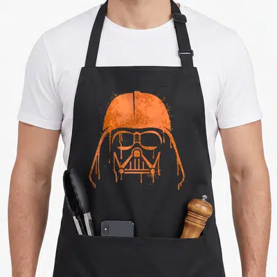 Tablier de cuisine noir avec illustration casque Dark Vador en peinture orange déformée et giclée.