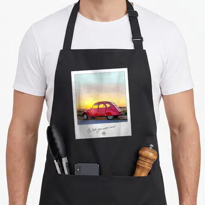 Tablier de cuisine noir avec une illustration polaroid d'une 2CV rouge au coucher du soleil et le texte Wish you were here en bas.