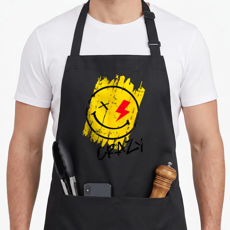 Tablier de cuisine noir avec un visage jaune sourant, un éclair rouge et le mot Crazy en bas.