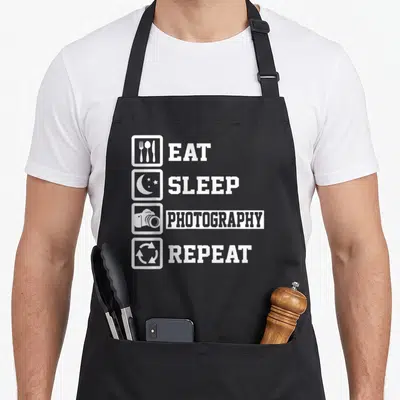 Tablier de cuisine noir avec les mots Eat Sleep Photography Repeat et quatre icônes blanches alignées verticalement.