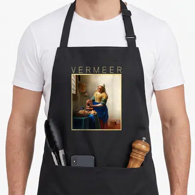 Tablier de cuisine noir avec reproduction d'une femme versant du lait et le nom Vermeer en lettres dorées au-dessus.