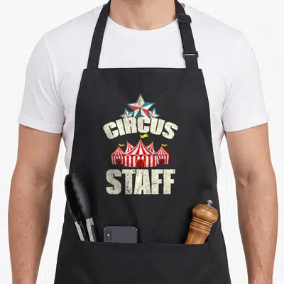 Tablier de cuisine noir avec illustration de tente de cirque et texte Circus Staff en blanc vieilli.