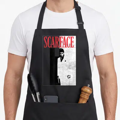 Tablier de cuisine noir avec affiche Scarface en noir et blanc et titre rouge, homme en costume blanc tenant un pistolet.