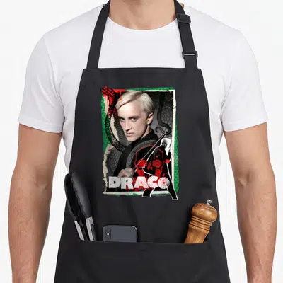 Tablier de cuisine noir avec collage artistique Draco Malfoy, serpent vert et texte blanc DRACO en bas.