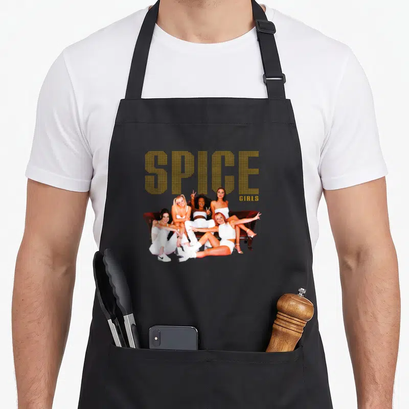Tablier de cuisine noir avec cinq femmes en blanc assises sur un canapé rouge et le texte Spice Girls en lettres dorées.