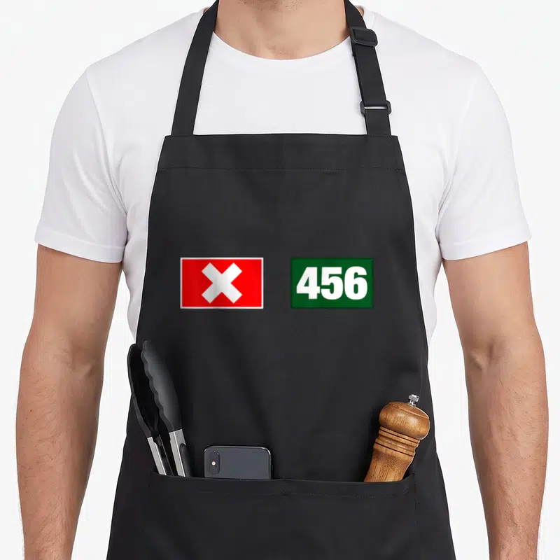 Tablier de cuisine noir avec un rectangle rouge à croix blanche et un rectangle vert affichant le nombre 456 en blanc.