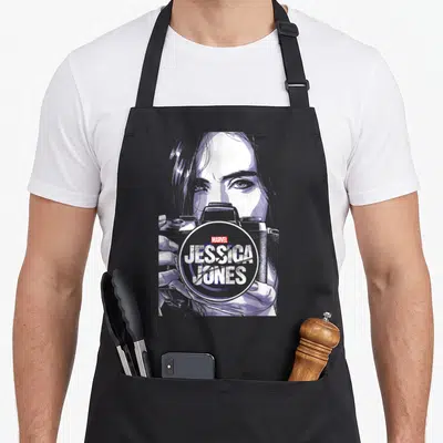 Tablier de cuisine noir avec illustration de Jessica Jones tenant une caméra et le logo Marvel.