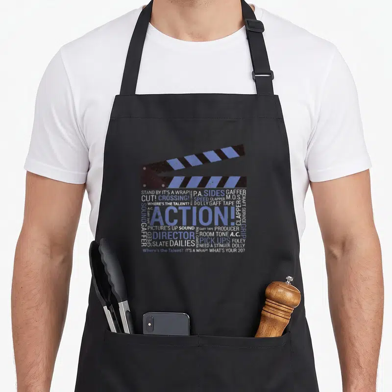 Tablier de cuisine noir avec une illustration de clapperboard bleue et noire et du texte blanc sur fond gris uni.