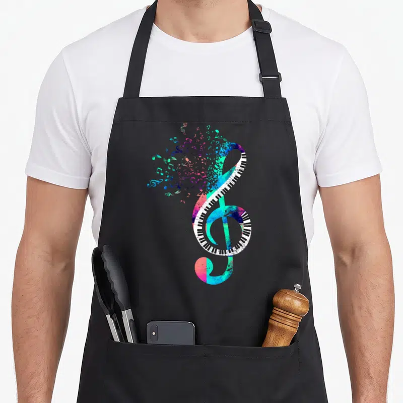 Tablier de cuisine noir avec une clé de sol stylisée en touches de piano multicolores et notes dispersées.