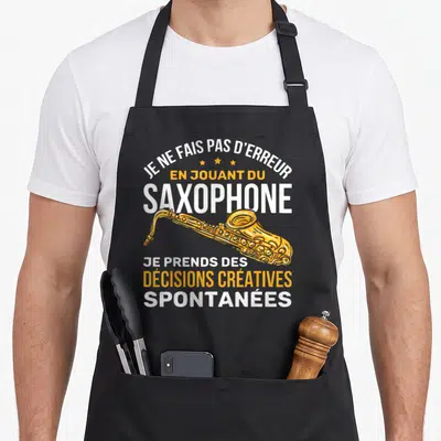 Tablier de cuisine noir avec illustration d'un saxophone doré et texte blanc et orange sur fond uni.