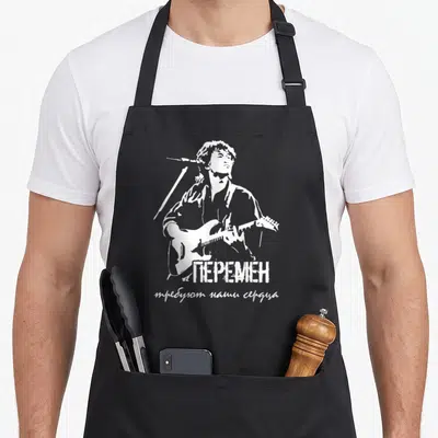 Tablier de cuisine noir avec illustration blanche de Viktor Zoi jouant de la guitare sous un micro, surmontée du texte EN en lettres capitales russes.