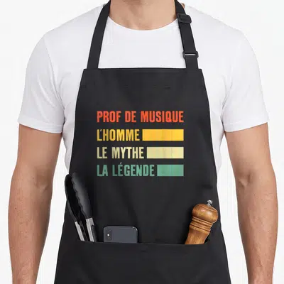 Tablier de cuisine noir avec inscription colorée « Prof de musique l'homme le mythe la légende » sur fond uni.