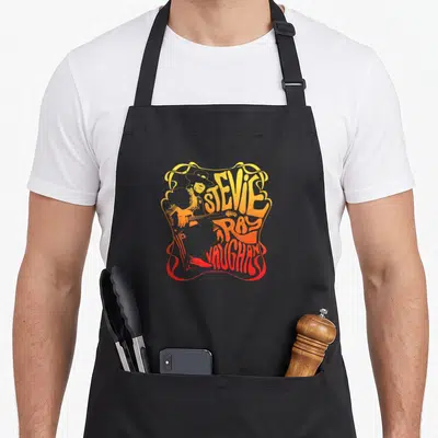 Tablier de cuisine noir avec illustration orange et rouge de Stevie Ray Vaughan jouant de la guitare.
