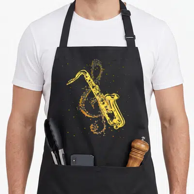 Tablier de cuisine noir avec saxophone jaune et clé de sol stylisée en motifs géométriques dorés sur fond gris.