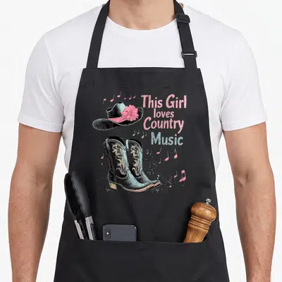 Tablier de cuisine noir avec bottes cowboy, chapeau fleurie et texte This Girl loves Country Music entouré de notes roses.