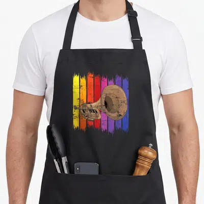Tablier de cuisine noir avec illustration de trompette dorée sur bandes de couleurs vives verticales.