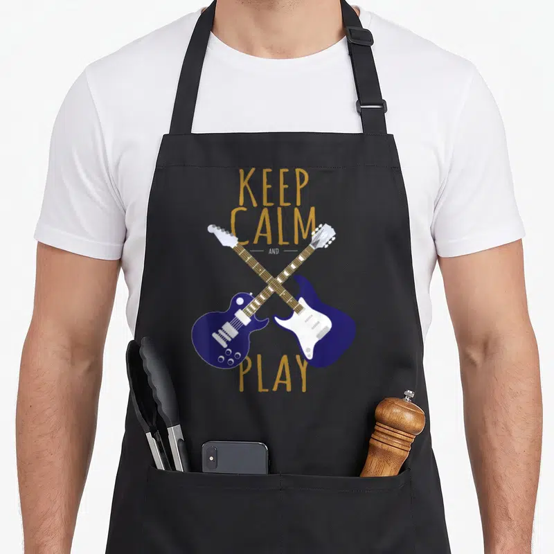 Tablier de cuisine noir avec deux guitares électriques bleues croisées et le texte Keep Calm And Play en lettres dorées.