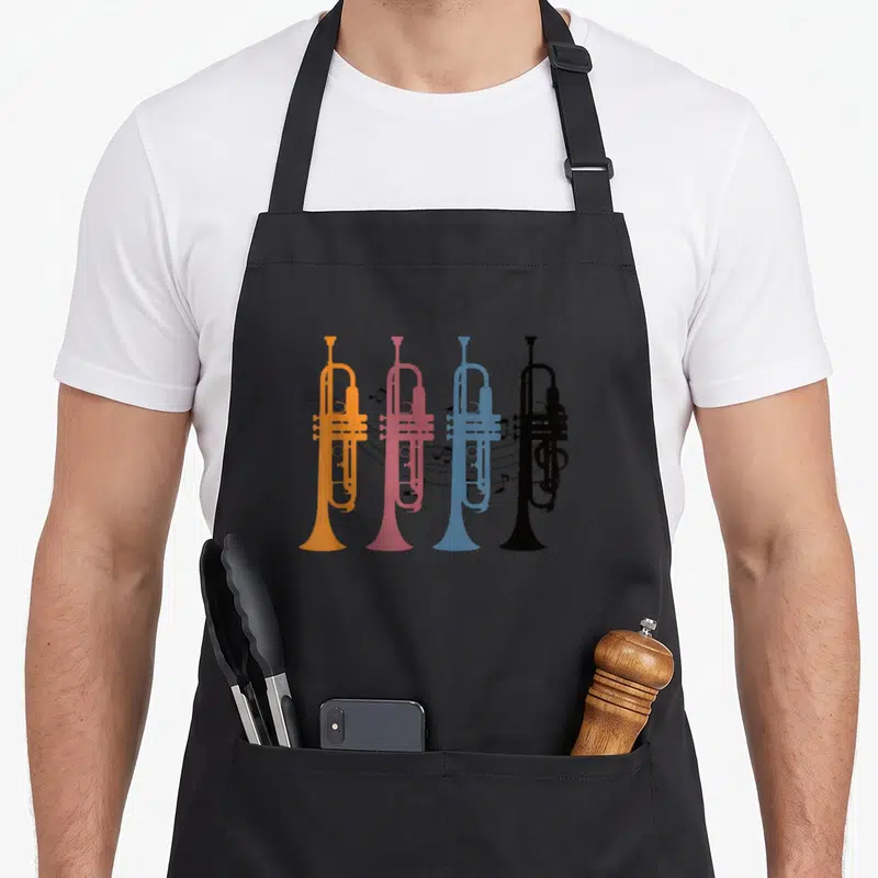 Tablier de cuisine noir avec quatre trompettes orange, rose, bleue et noire sur fond gris uni.