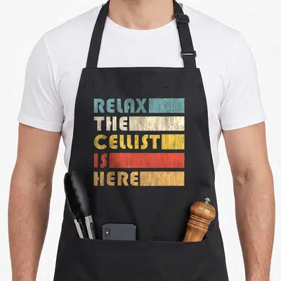 Tablier de cuisine noir avec texte Relax The Cellist Is Here en lettres colorées style rétro.