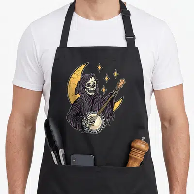 Tablier de cuisine noir avec un squelette capuchon jouant du banjo devant une lune jaune et des étoiles dorées.