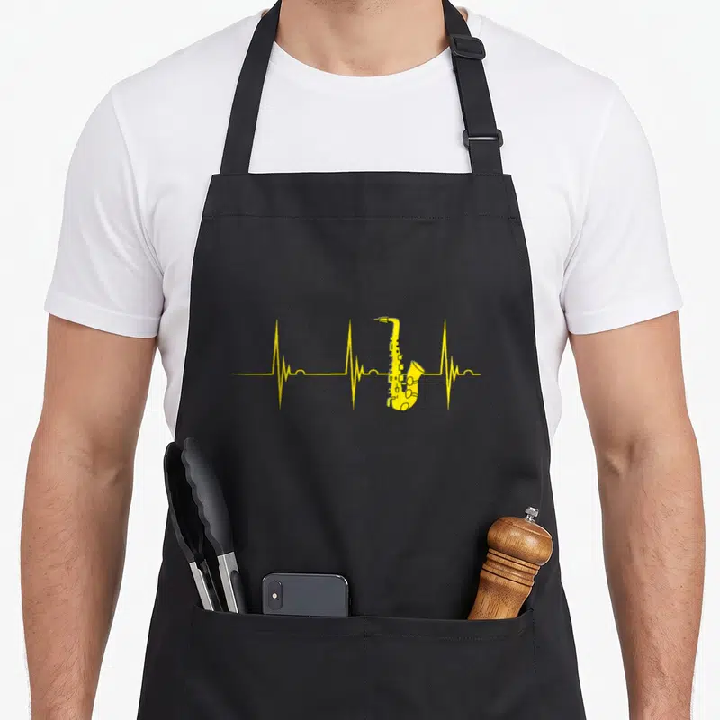 Tablier de cuisine noir avec un saxophone alto jaune formant une ligne de battement de cœur stylisée.